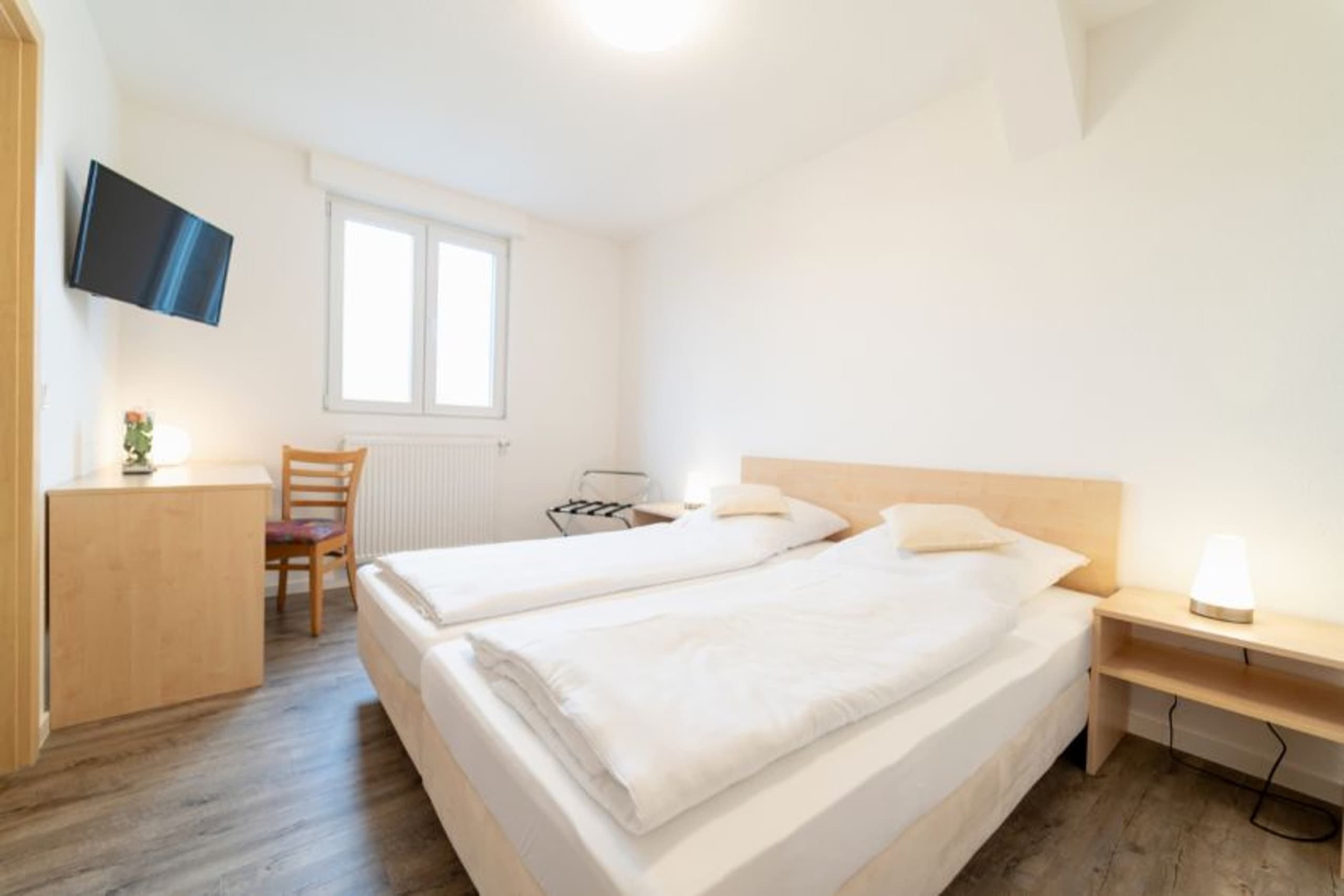Helles Hotelzimmer mit zwei Einzelbetten, Holzboden, Schreibtisch und Wandfernseher.